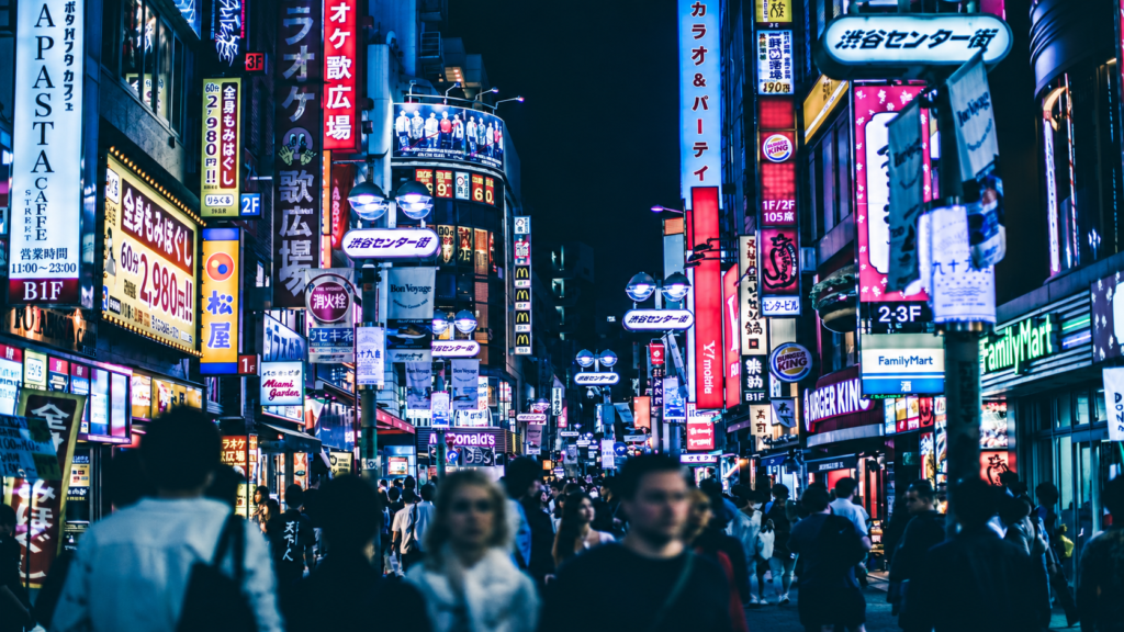 Crowded Tokyo street at night with bright neon signs, storefronts and blurred pedestrians in Shibuya.
